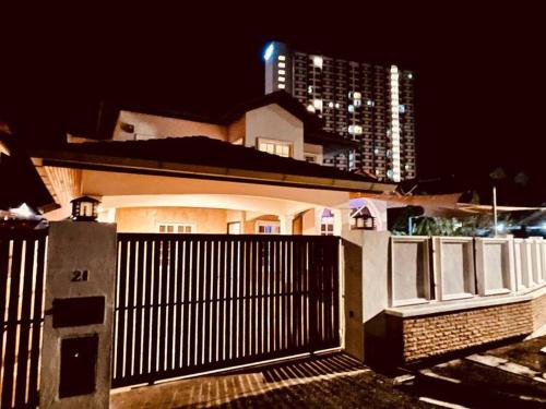 a white house with a fence and a tall building at Trendy Family Getaway by StayCo - Mini-Pool, Outdoor Cinema, Air Loft, PS4, KTV - Just 2 mins to Beach! in Batu Ferringhi