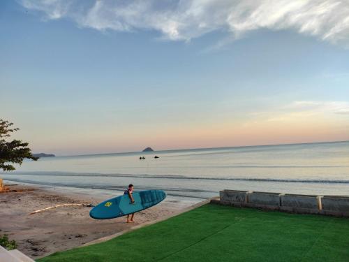 a person holding a blue surfboard on the beach at Talaytime Pool Villa in Laem Sing