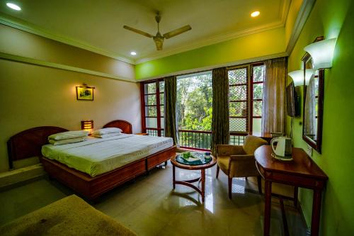 a bedroom with a bed and a table and window at Aranya Nivas in Thekkady