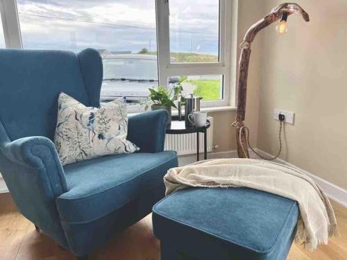 a blue chair and a stool in a room with a window at Donegal Beach Cottage with Sea Views, sleeps six in Lettermacaward