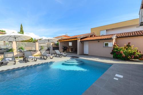 a swimming pool with chairs and umbrellas next to a house at Villa Jolanda in Umag