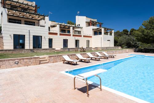 a swimming pool with lounge chairs and a building at Aphaia Villa & Residences Aegina in Agia Marina Aegina