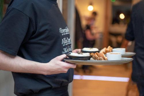 a man holding a plate of food with cups and pastries at The Woodside in Doune