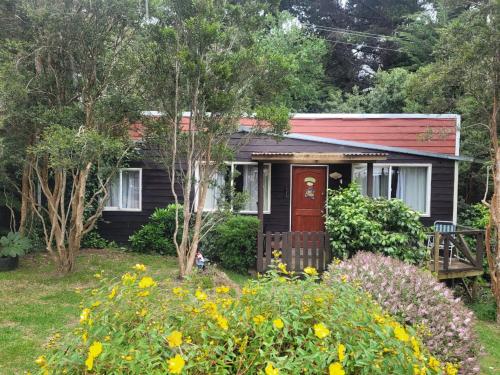 a small house with a red door in a yard at CABAÑAS ISITEPUAL 5 min aeropuerto y 10 min del centro in Puerto Montt