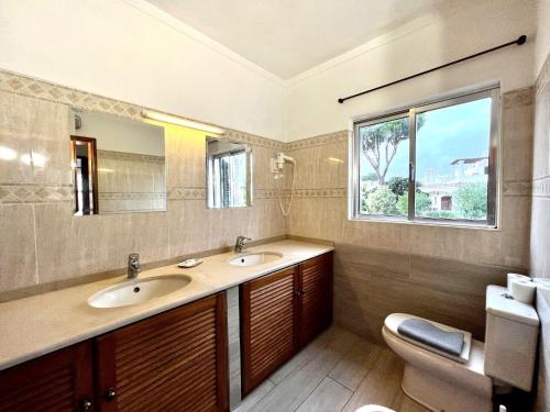 a bathroom with two sinks and a toilet and a window at Vilamoura Ocean Villa with Pool by Homing in Vilamoura
