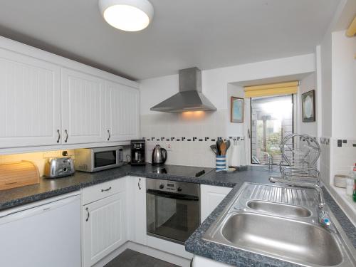 a kitchen with white cabinets and a stainless steel sink at Pass the Keys Comfortable Stone Built Cottage in Menai Bridge in Menai Bridge