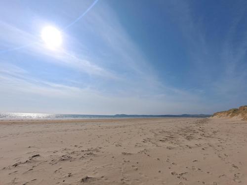 a sandy beach with the sun in the sky at Pass the Keys 2 Bed Sea View Apartment with Balcony Parking in Benllech