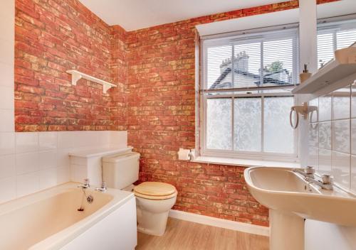 a bathroom with a brick wall and a toilet and a sink at Greyhound Cottage in Kendal