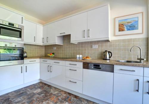 a white kitchen with white cabinets and a sink at Cornerways in Worth Matravers