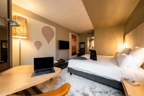 メランにあるMercure Grenoble Meylanのベッド、デスク、ノートパソコンが備わるホテルルームです。