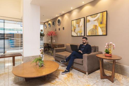 a man sitting on a couch in a waiting room with a laptop at Tulip Inn Vila Velha in Vila Velha