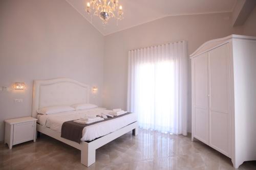 a white bedroom with a bed and a chandelier at B&B Royal in Sellia Marina