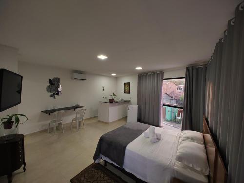 a bedroom with a bed and a desk and a kitchen at Flats Paraíso Louveny in Japaratinga