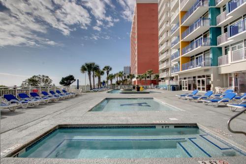 a swimming pool with chairs and a building at Sunny and Bright Oceanfront Condo in Atlantica Resort near Boardwalk in Myrtle Beach