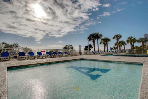 a swimming pool with blue chairs and palm trees at Sunny and Bright Oceanfront Condo in Atlantica Resort near Boardwalk in Myrtle Beach