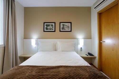 a bedroom with a bed with white sheets and two lamps at Interclass Florianópolis in Florianópolis