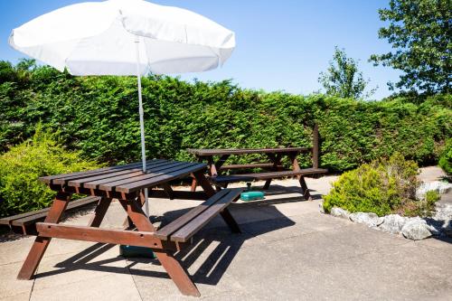a picnic table with an umbrella and two benches at The Runmere Hotel, Part of AG Collection in Runcorn