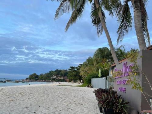 einen Sandstrand mit Palmen und ein rosafarbenes Gebäude in der Unterkunft Bella Vista Beach Resort Koh Lipe in Ko Lipe