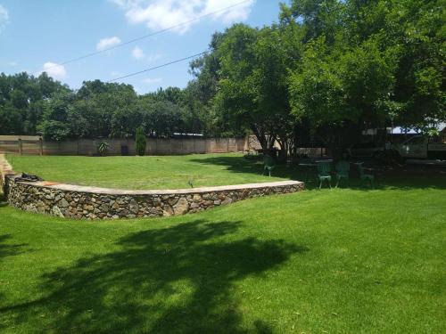a grassy yard with a stone wall and trees at LightStone Guesthouse in Centurion
