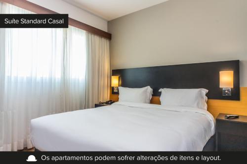 um quarto com uma grande cama branca e uma janela em Paraíso Suítes by Charlie em São Paulo