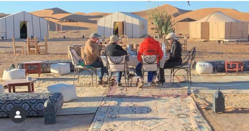 a group of people sitting at a table in the desert at Peace of mind camp in Mhamid