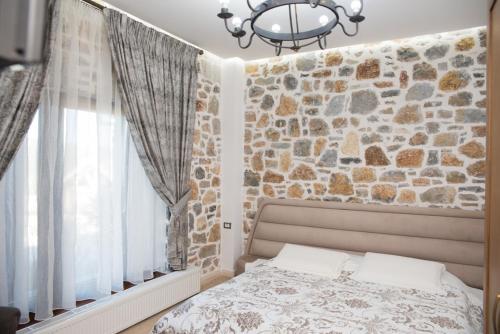a bedroom with a stone wall with a bed and a chandelier at Luxury Villa Saint Nikolas in Voskopojë