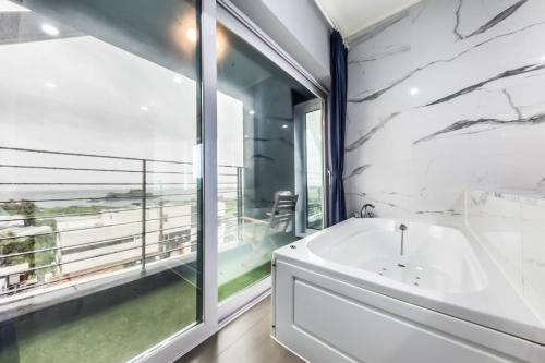 baño con bañera blanca y ventana grande en Gladsheim Hotel, en Seogwipo