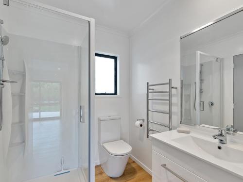 a white bathroom with a toilet and a glass shower at Mangawhai Monarch - Mangawhai Heads Holiday Home in Mangawhai
