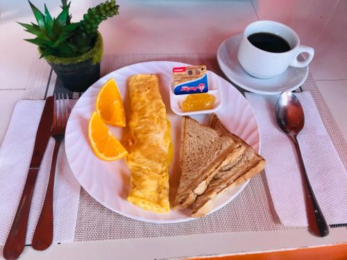 einen Teller mit einem Sandwich und orangefarbenen Scheiben und einer Tasse Kaffee in der Unterkunft SunValley Tourist Inn in Coron