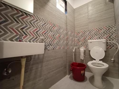 a bathroom with a toilet and a red bucket at Royal N Deluxe in Bangalore