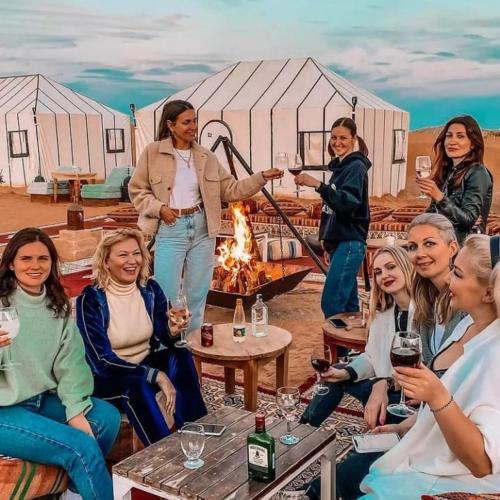 a group of women sitting around a fire in front of a tent at Desert Lover's Luxury Camp in Merzouga