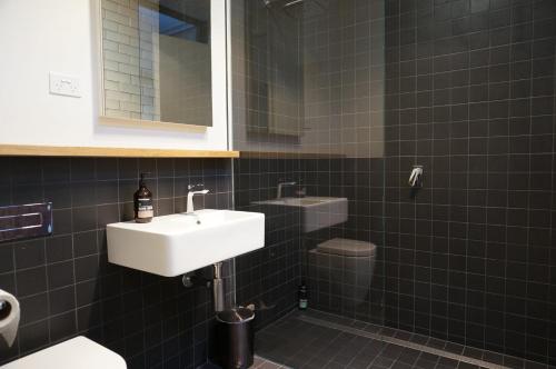 a black tiled bathroom with a sink and a toilet at Stella on Stevens in Queenscliff