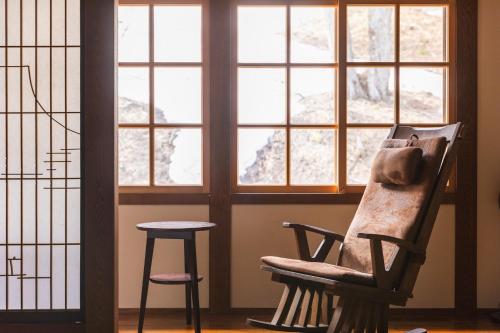 una silla y un taburete en una habitación con ventanas en Tsuta Onsen Ryokan, en Towada