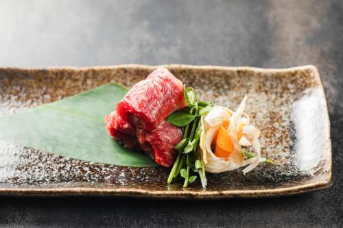 a piece of meat on a plate with vegetables at Tsuta Onsen Ryokan in Towada