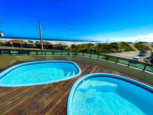 a swimming pool on top of a deck with the ocean at Loft Luxo Vista Mar Orla Praia Grande in Arraial do Cabo