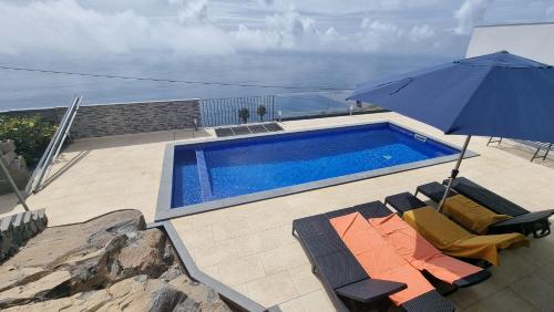 una piscina con sombrilla y algunas sillas en Majestic Seaview Villa, en Fajã da Ovelha