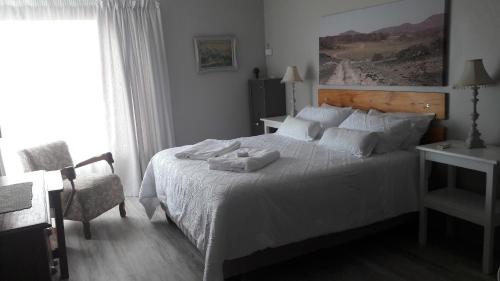 a bedroom with a white bed with a chair and a window at TOEVLUG in Gansbaai