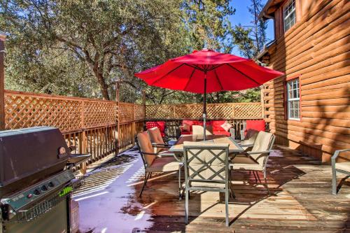 a patio with a table with a red umbrella and a grill at Pine Mountain Club Log Home with Deck and Grill! in Pine Mountain Club