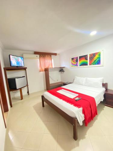a bedroom with a bed with a red blanket and a tv at Hotel La Guajira in Ríohacha