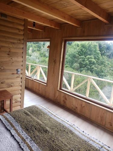 a bedroom with two large windows in a log cabin at Cabañas Vasconia in Castro