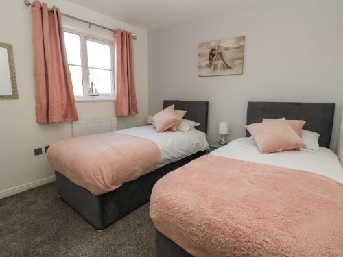 a bedroom with two beds with pink pillows and a window at The Beach House in Prestatyn