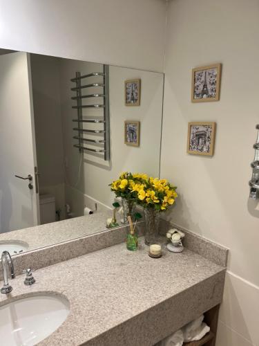 a bathroom with a sink and a vase of yellow flowers at Flat Completo Granja Brasil in Petrópolis