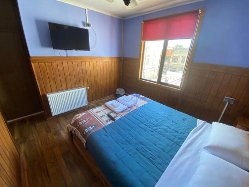 a bedroom with a bed with a blue comforter and a television at Hostal Ochen in Punta Arenas