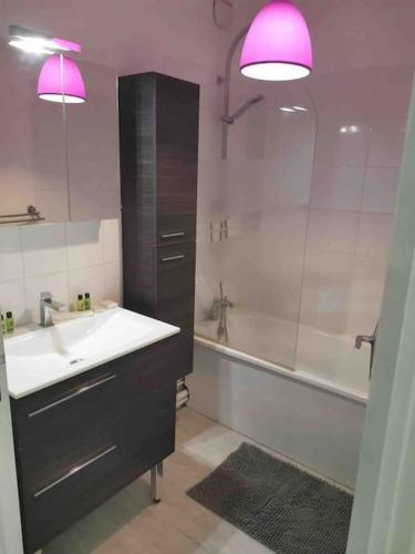 La salle de bains est pourvue d'un lavabo, d'une baignoire et de lumières roses. dans l'établissement Charmant appartement au calme, à Bourg-en-Bresse