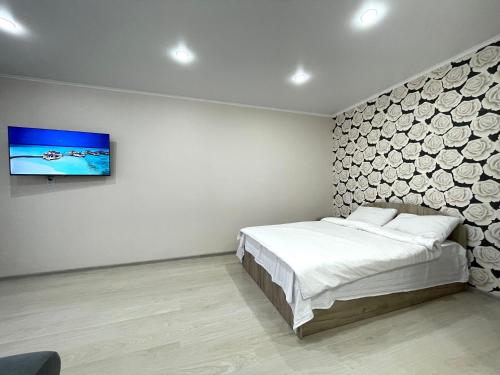 Un dormitorio con una cama y un televisor en una pared. en Квартира DOSTYK MALL, Университет, en Petropavlovsk