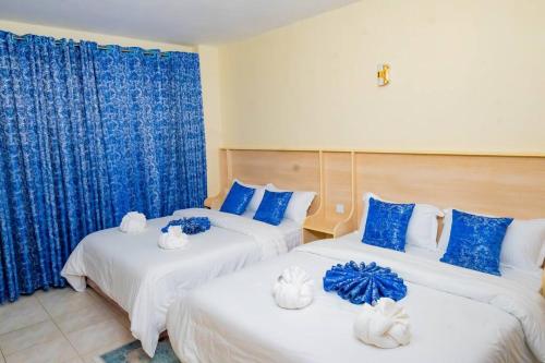 two beds in a room with blue curtains at GreenLea Nanyuki: 2 Bedroom Apartments in Nanyuki