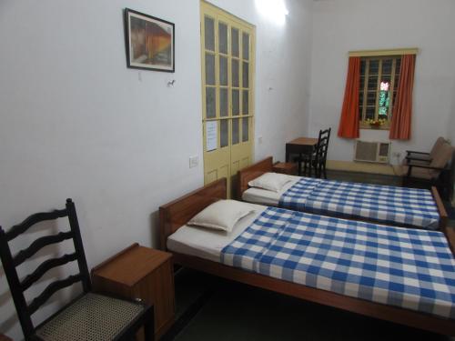 a bedroom with two beds and a chair and a window at YWCA GALLWAY GUEST HOUSE in Kolkata