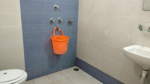 an orange bucket in a bathroom with a toilet and sink at YWCA GALLWAY GUEST HOUSE in Kolkata