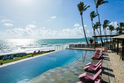 a swimming pool with lounge chairs and the ocean at Vila do Mar Natal - All Inclusive in Natal