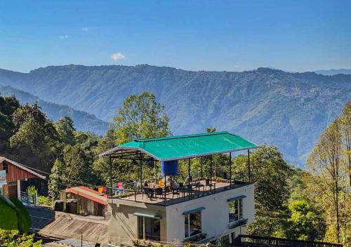 a house with a green roof with mountains in the background at The Oak Retreat Lamahatta in Darjeeling
